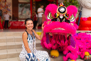 A European tourist girl at a Chinese New Year celebration in a Chinese temple is photographed with a traditional Chinese dragon. Festive Chinese entertainment