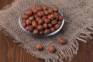 Hazelnuts in a glass plate close-up on burlap and wooden background