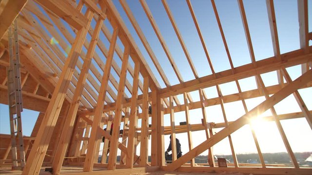 Sliding view of wooden beams of roof and walls of unfinished frame house with blue sky on the background. Working builders. Beautiful natural light, sunny day