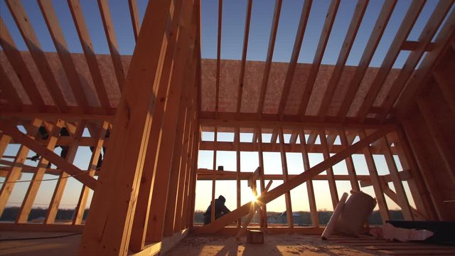 Timelapse, view from below of unfinished frame house interior and builders covering roof with waterproofing layer. Sunny day