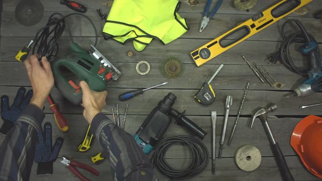 A variety of electro and hand tools and special clothing. Top view. Slow motion.  The male hand takes an electric jigsaw from the table and after a while puts it back.