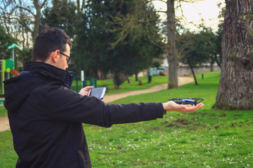 A boy holding a drone in his hand with a smartphone as a remote control in an outdoor park. Small aircraft without crew. 