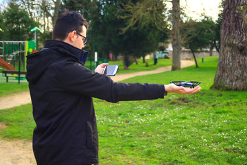 A boy holding a drone in his hand with a smartphone as a remote control in an outdoor park. Small aircraft without crew. 