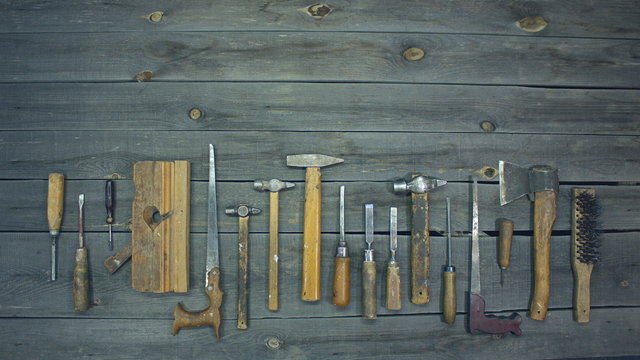 Old hand tools. Top view.  On the table are laid out old instruments with wooden handles: screwdrivers, chisels, hand saws, hammers, ax, awl, metal brush, jointer.