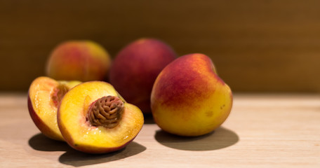 Durazno partido a la mitad en primer plano. Conjunto de duraznos frescos y deliciosos detrás. Frutas de estación aisladas con fondo de madera detrás y luz cálida sobre ellos. 