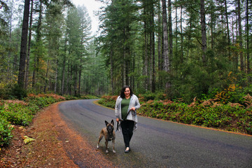 ethnic middle aged woman walking large dog in foggy forest