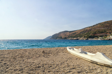 Fototapeta na wymiar Active rest, sport, kayak. Single white kayak stand on a stony beach on the seashore of the Albanian Riviera.
