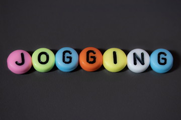 The word JOGGING written on colorful beads isolated on a dark background...