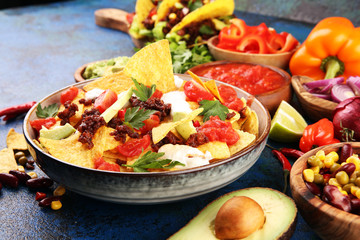 mexican nacho chips garnished with ground beef, guacamole, melted cheese, peppers and cilantro leaves in plate
