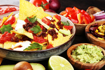 mexican nacho chips garnished with ground beef, guacamole, melted cheese, peppers and cilantro leaves in plate