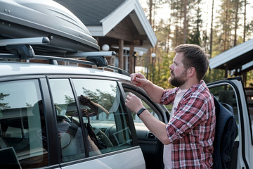 Serious, bearded man with a backpack holds the keys in hand and is about to open the roof rack of...