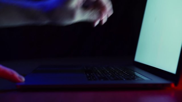 Closeup man sitting table notebook. Hands keyboarding laptop using texting pointing networking white screen. Neon glow of blue, red and green.