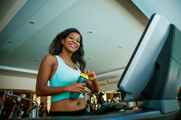 fitness center lifestyle portrait of young happy and attractive black African American woman at gym running on treadmill machine smiling cheerful walking warming up in sport concept