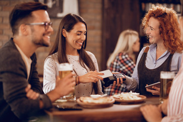 Young woman using smart phone while paying a bill in a pub.
