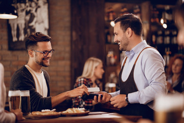 Young happy man making mobile payment in a pub.