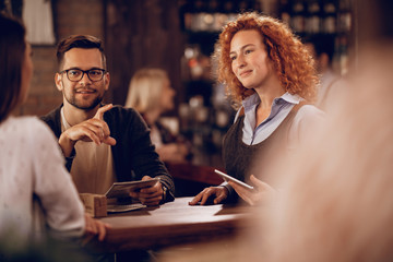 Young waitress taking an order form a couple in a pub.
