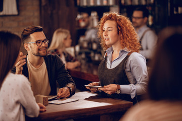 Young waitress communicating with a couple while taking their order in a bar.