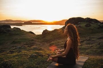 Woman doing yoga alone at sunrise with mountain and ocean view. Harmony with nature. Self-analysis and soul-searching