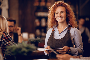 Portrait of young happy waitress with digital tablet in a bar.