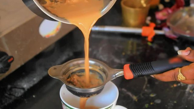 Real time shot of hot homemade tea or chai being strained on to a cup on a kitchen shelf.