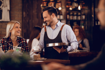 Young happy waiter serving a female guest in a cafe,