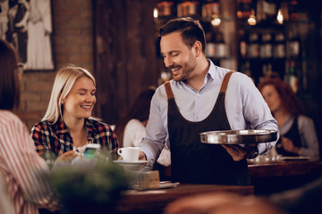 Happy waiter serving his guests with a coffee in a cafe,