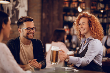 Young cheerful waitress serving beer to her guests in a bar.