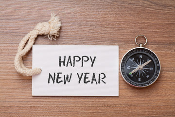 Happy New Year written on label with Compass on wood background