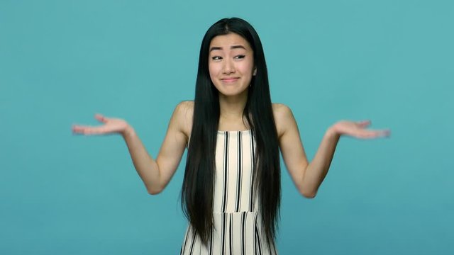 I don't know. Confused asian woman with long straight black hair in dress raising hands in questioning gesture, gazing around with puzzled helpless face. indoor studio shot isolated on blue background