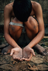 poor child or beggar begging you for help sitting at dirty slum. concept for poverty or hunger people,human rights,donate and charity for underprivileged children in third world 