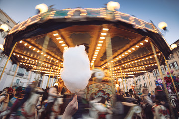 Portrait of a beautiful young girl with white cotton candy in front of a carousel horse