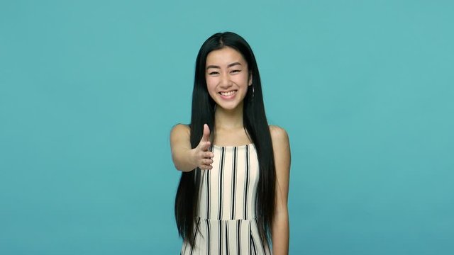 Cheerful asian woman with long straight black hair giving hand to handshake and smiling with friendly hospitable expression, welcoming or getting acquainted. studio shot isolated on blue background