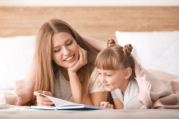 Beautiful young woman and her little daughter reading book at home