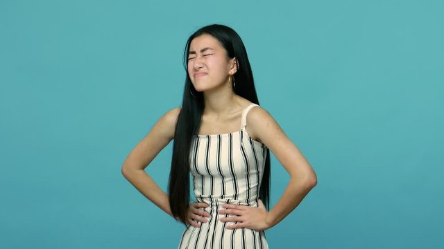 Severe abdominal pain. Sick asian woman with long hair clutching painful belly, suffering stomach ache of indigestion, spasm or cramps, medical problem. indoor studio shot isolated on blue background