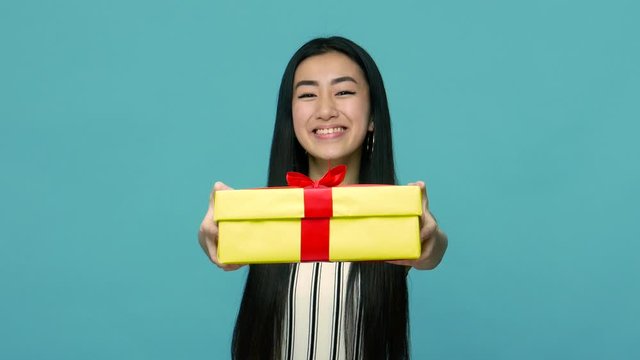 Take it, surprise for you! Friendly generous asian woman with long hair giving wrapped gift box to camera, greeting with birthday and offering present. indoor studio shot isolated on blue background