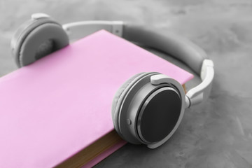 Book and modern headphones on grey background. Concept of audiobook