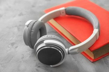 Book and modern headphones on grey background. Concept of audiobook