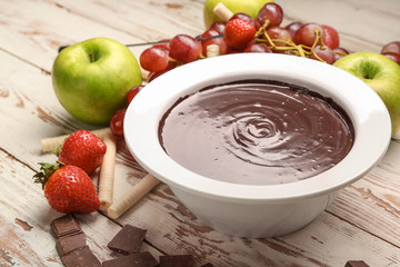 Bowl with tasty chocolate fondue and fruits on table