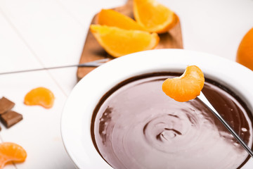 Dipping of tasty tangerine into bowl with chocolate fondue on table, closeup