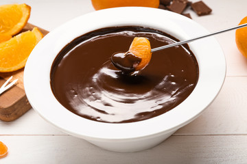 Dipping of tasty tangerine into bowl with chocolate fondue on table