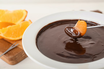 Dipping of tasty tangerine into bowl with chocolate fondue on table, closeup