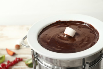 Dipping of tasty marshmallow into bowl with chocolate fondue on table, closeup