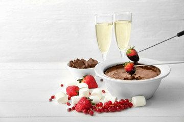 Dipping of tasty strawberry into bowl with chocolate fondue on table