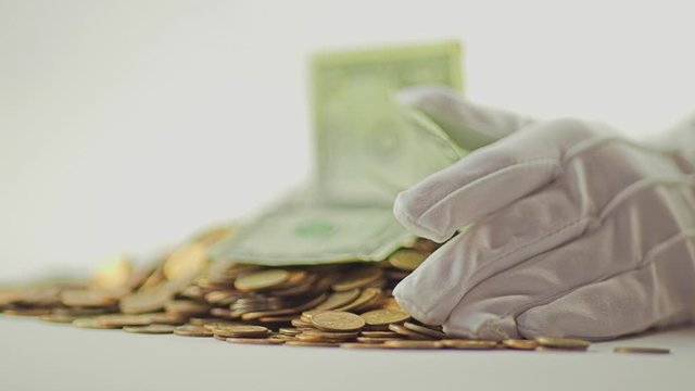 White-gloved hands scooping up a pile of gold coins. They sort out and scatter money.On white background. Garland. Money glitters.