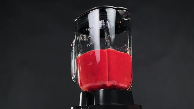 Slowmotion of a fruit blender mixing cold strawberry smoothie on a black background. Fruit mixer making juice. Making sweet healthy delicious drink from strawberries. 