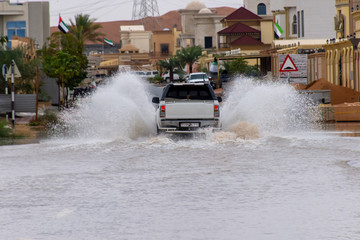 Truck driving through flood waters on the street making large splashes of water in a residential area.