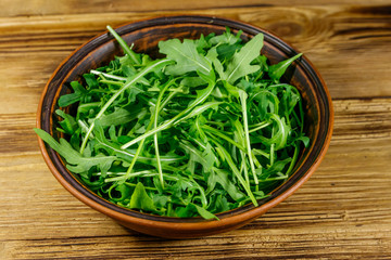 Fresh green arugula in ceramic bowl on a wooden table. Healthy food or vegetarian concept