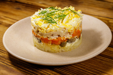 Tasty layered salad with potatoes, chicken breast, marinated mushrooms, carrots, eggs and mayonnaise on wooden table
