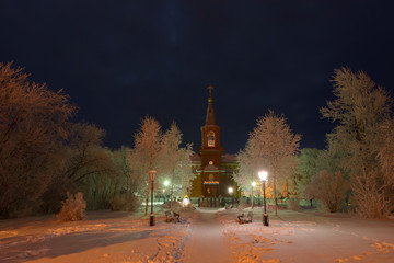 The building of the Orthodox Church at night surrounded by trees in the snow.