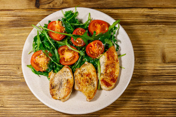 Fried chicken breast with salad of fresh arugula and cherry tomatoes on wooden table. Top view